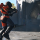 One spartan fires a needler at another in a gray stone hallway in Halo Infinite.